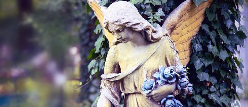 Vintage image of a sad angel against the background of leaves (fragment)