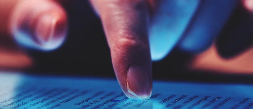 Extreme close up of female finger using digital tablet computer at home in the evening to read the news online, selective focus