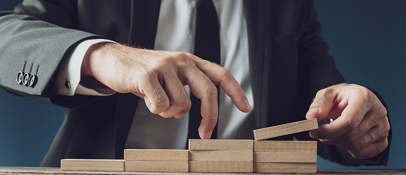 Businessman assembling stairway of wooden pegs as he walks his fingers upwards in a conceptual image.