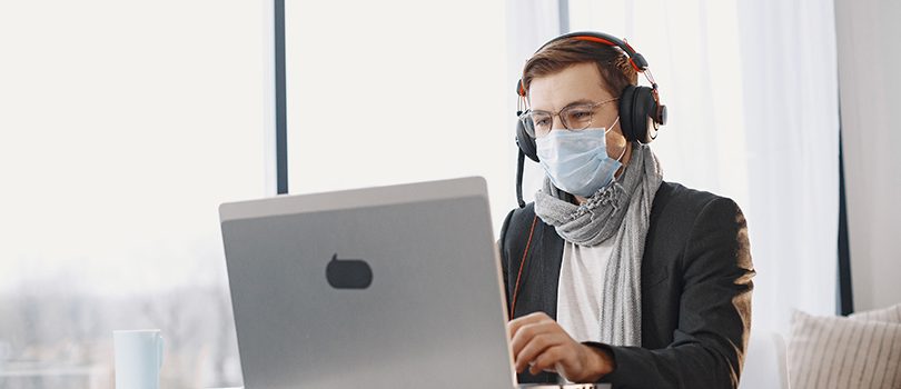 Male in a medical mask. Man sitting in living room at home. Guy enjoying studying on quarantine.