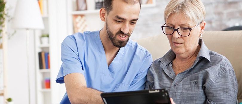 Health visitor helping senior woman to use tablet in nursing home.