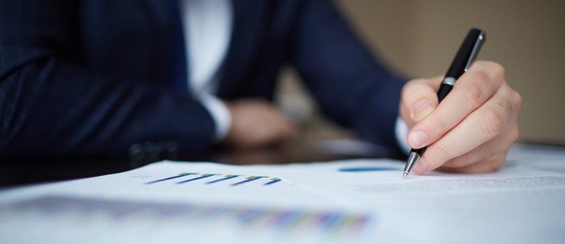 Image of human hand with pen over documents at workplace