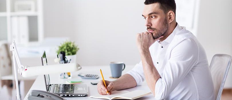 business and people concept - businessman with laptop and notebook sitting at office table and thinking