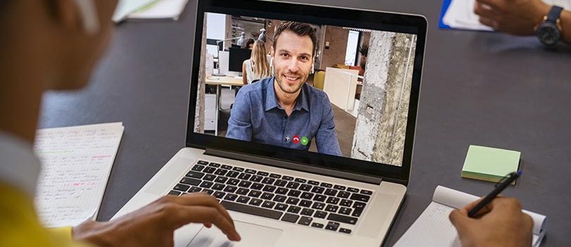 Smiling business partners talking through video call. Back view of african businessman in office doing video chat calling a client. Young man and his business colleague talking to each other through a video conference on digital tablet screen.