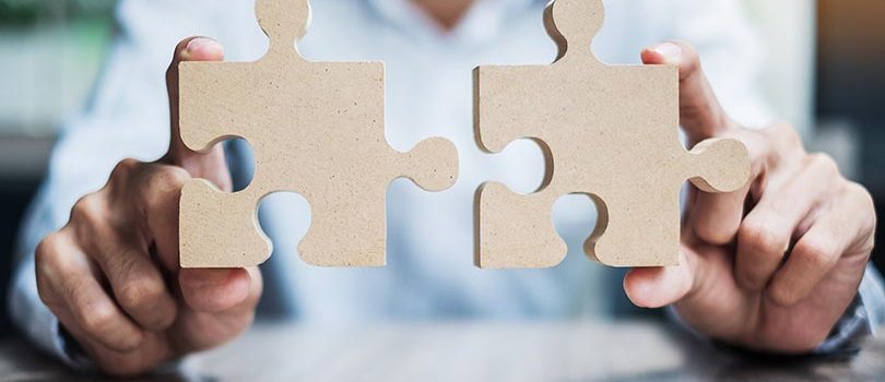 man hands connecting couple puzzle over table, businessman holding wood jigsaw inside office. Business solutions, mission, target, success, goals and strategy concepts